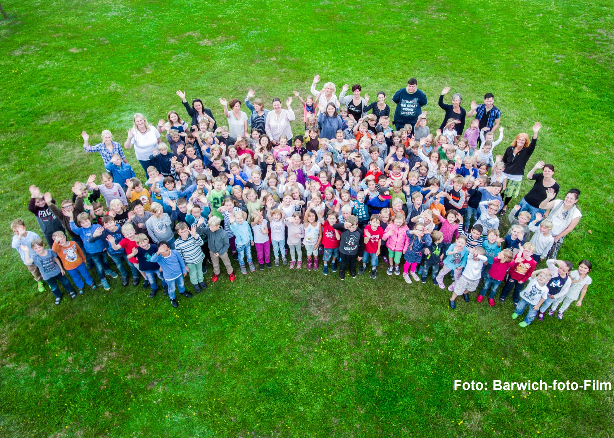 Kinder und Mitarbeitende der Grundschule Ashausen winken auf dem Schulgelände in die Kamera