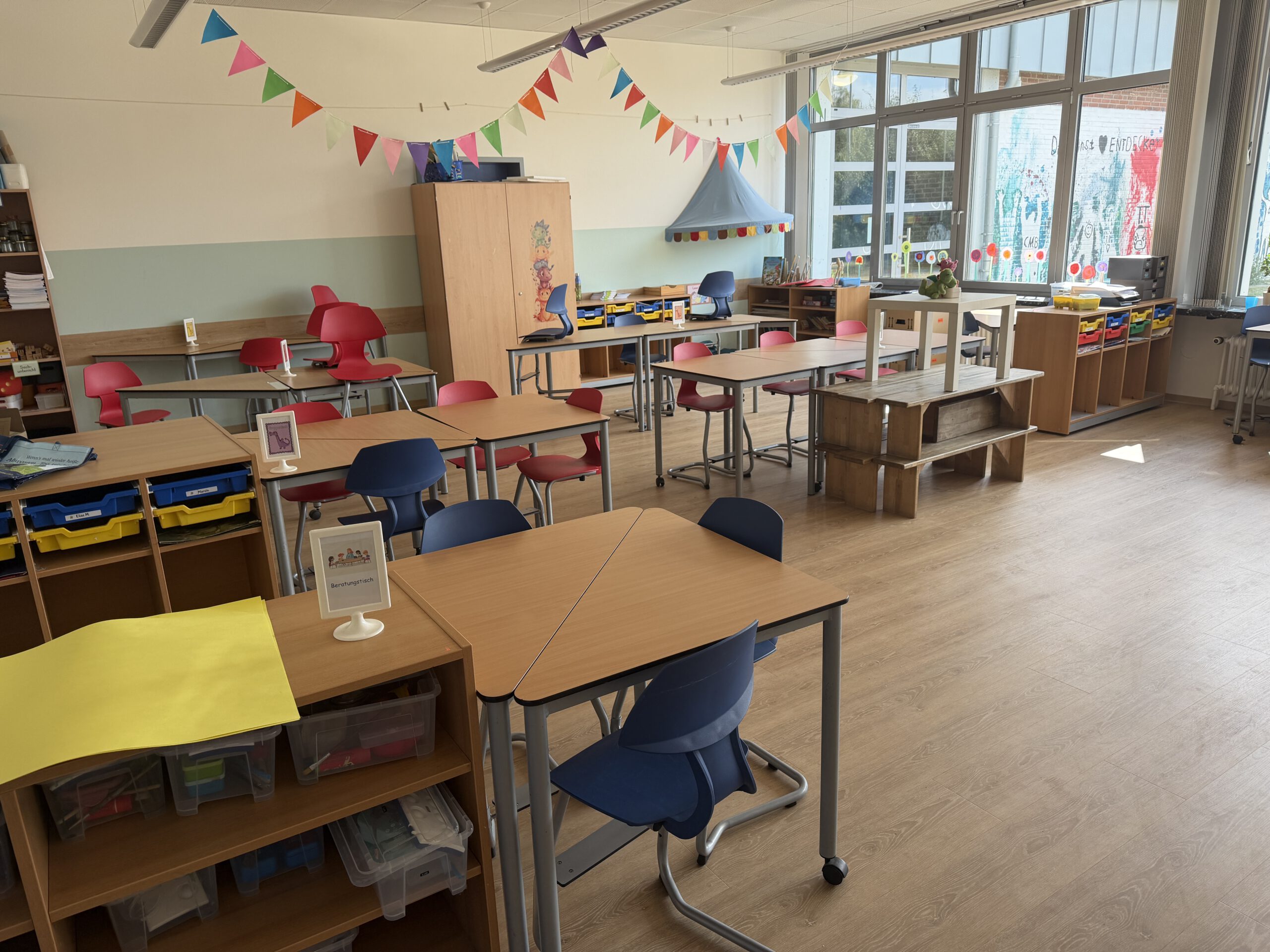 Heller Klassenraum der Grundschule Ashausen mit Tischgruppen, Stauraumfächern und Sitzmöglichkeiten.